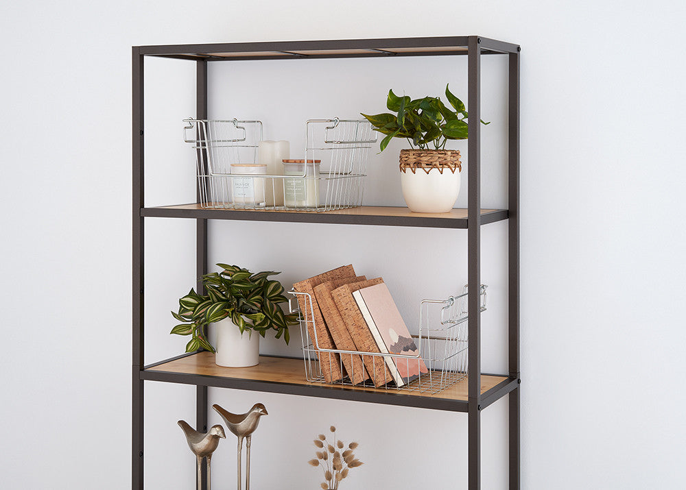A modern metal and wood bookshelf against a white wall, featuring decorative elements such as potted plants, wire baskets, candles, books, and small brass bird figurines. The neatly arranged items create a minimalist and stylish aesthetic.