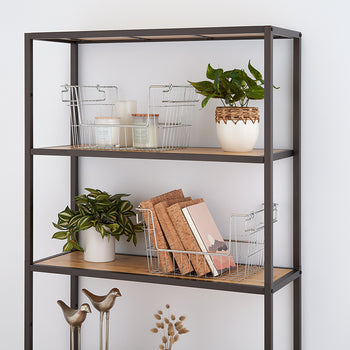 A modern metal and wood bookshelf against a white wall, featuring decorative elements such as potted plants, wire baskets, candles, books, and small brass bird figurines. The neatly arranged items create a minimalist and stylish aesthetic.