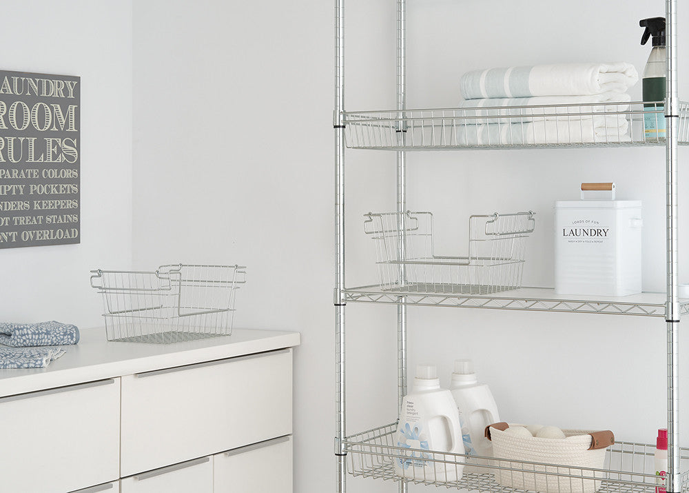 A well-organized laundry room features a metal shelving unit stocked with neatly folded towels, detergent bottles, a laundry container, and wire baskets. A white cabinet with drawers sits below a wall sign displaying "Laundry Room Rules."