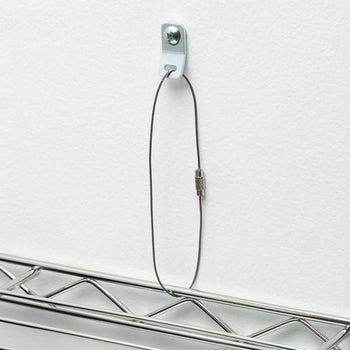 A thin, dark brown wire is looped around a chrome wire shelf, extending upwards to a small, white metal bracket screwed into a white wall. The wire is secured by a small, textured metal barrel near the top of the loop.