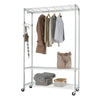 A chrome wire clothing rack on wheels is shown against a white background. Several garments hang from the top bar, and shelves below hold a tote bag, a box with a blanket, and a small woven basket.