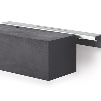 A black, wood-textured floating mantel is shown being slid onto a silver metal wall-mounting bracket. The bracket is secured to a white wall, and a small pre-drilled hole is visible on the top surface of the mantel for final fastening.