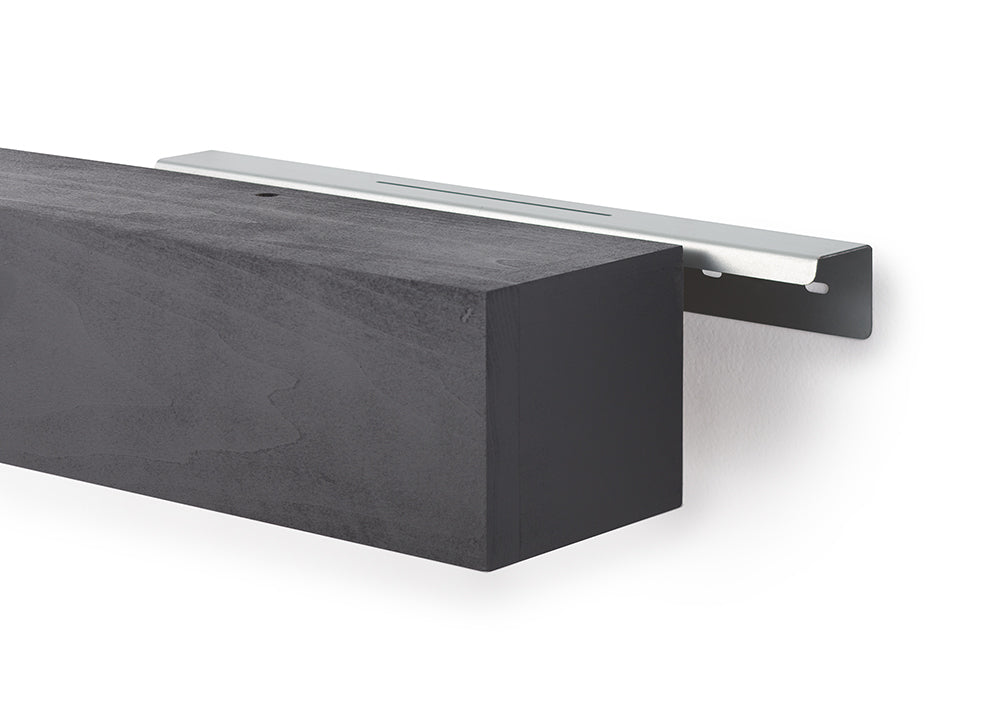 A black, rectangular floating mantel with a wood-grain texture is shown alongside its silver metal mounting bracket. The bracket is attached to a white wall, illustrating how the hollow mantel slides over the hardware for a concealed installation.