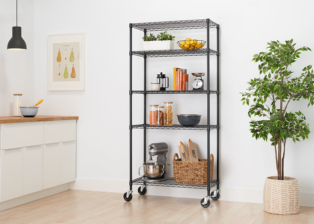 A five-tier black wire shelving unit with locking casters is shown, fully stocked with kitchen and home items. The shelves hold a stand mixer, a woven basket, glass storage containers, books, kitchen scales, and potted herbs and lemons.