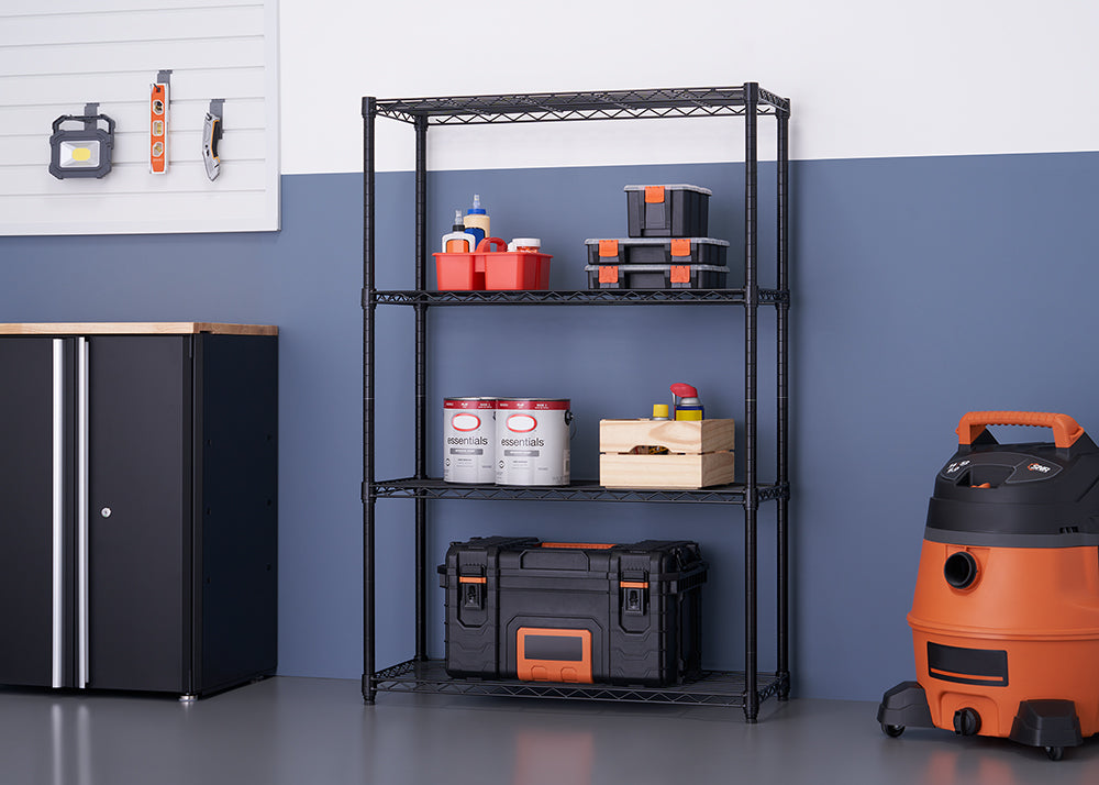 A four-shelf black wire rack is set up in a garage, holding various items like tools, paint cans, and storage bins. To the left is a black metal cabinet with a wood countertop, and to the right is a large orange and black shop vacuum.