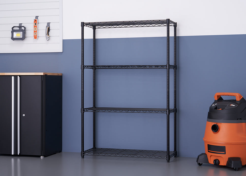 A close-up, eye-level shot shows a black metal, four-tier wire shelving unit. The unit is standing on a light gray concrete floor in what appears to be a clean garage with two-tone blue and white walls.