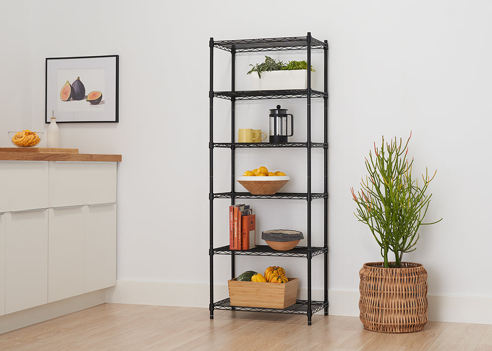A six-tier, black wire shelving unit is pictured, filled with kitchen and decorative items in a bright, modern room. Items include potted plants, a coffee press, a bowl of lemons, books, and gourds in a wooden crate.