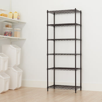 A tall wire shelving unit with five adjustable shelves stands against a white wall. The unit is in a room with light wood flooring, next to built-in white shelving on the left that holds clear and opaque storage containers.
