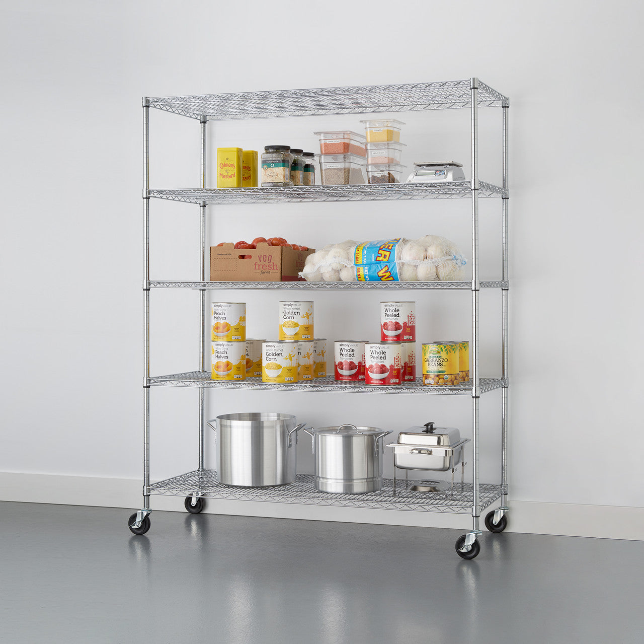 A tall, five-tier wire shelving rack with wheels stands against a white wall. The shelves hold various pantry items including canned goods, produce, and kitchen equipment.
