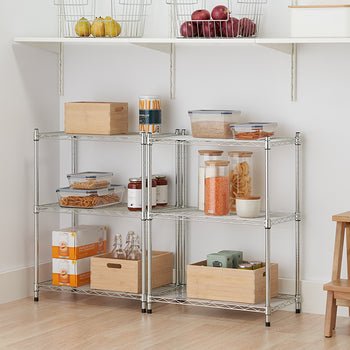 A low, three-tier chrome wire shelving unit holds various food items and storage containers in a pantry. Items on the shelves include glass jars of lentils and pasta, plastic containers of pretzels and crackers, and two wooden crates.