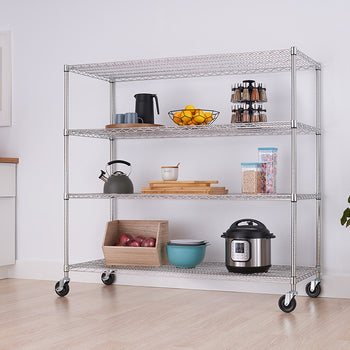 A four-tier wire shelving unit with wheels is shown in a bright, modern kitchen. The shelves hold various kitchen items, and the unit is positioned against a white wall with a framed picture and a potted plant nearby.