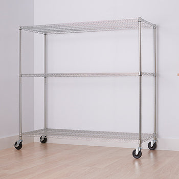 A three-tier wire shelving unit with wheels is shown in a room with light-colored walls and flooring. The unit is empty and positioned against a white wall, with a partial view of a white cart with a wooden top on the right.