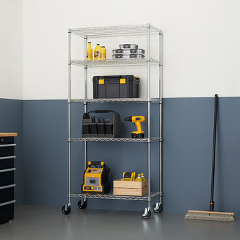 A chrome wire shelving unit with four shelves sits in a garage. The shelves are filled with tools and supplies, including a yellow and black toolbox, a tool bag, a cordless drill, a wooden crate with bottles, and a battery jumper box.