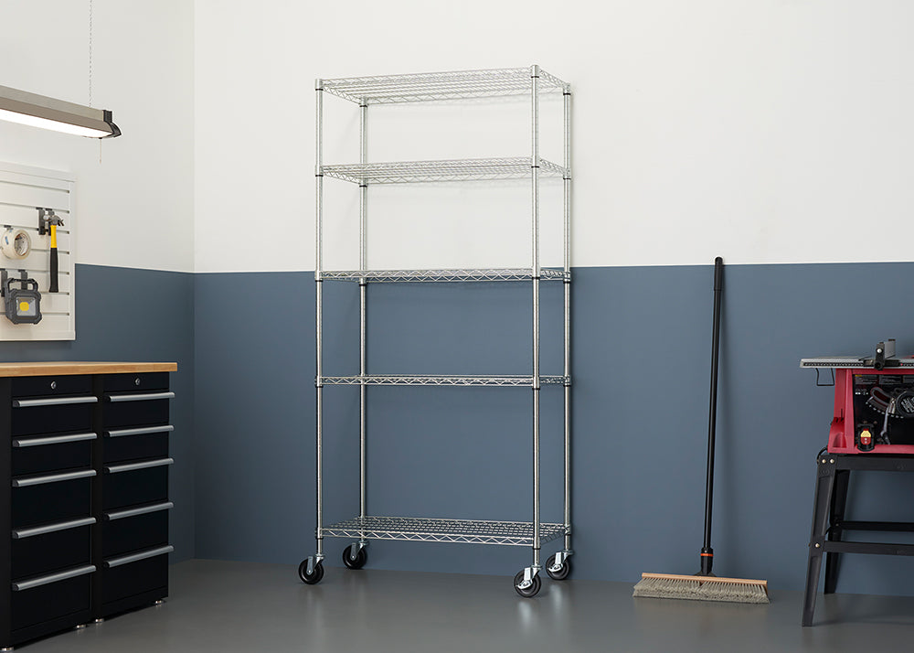 A chrome wire shelving unit with five shelves on casters is centered in a room with a two-toned wall. The bottom half of the wall is dark gray, and the top half is white.