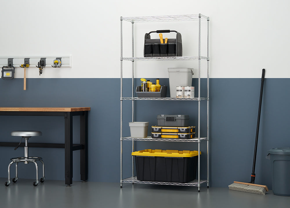 A tall, 5-tier chrome wire shelving unit is positioned against a wall in a workshop, fully stocked with storage bins, tool boxes, paint cans, and cleaning supplies. To the left, a portion of a workbench and a silver rolling stool are visible, along with wall-mounted tool storage.