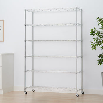 A six-shelf chrome wire rolling rack is shown centered against a white wall. To the right is a large potted plant, and to the left is a white cabinet with a framed print above it.