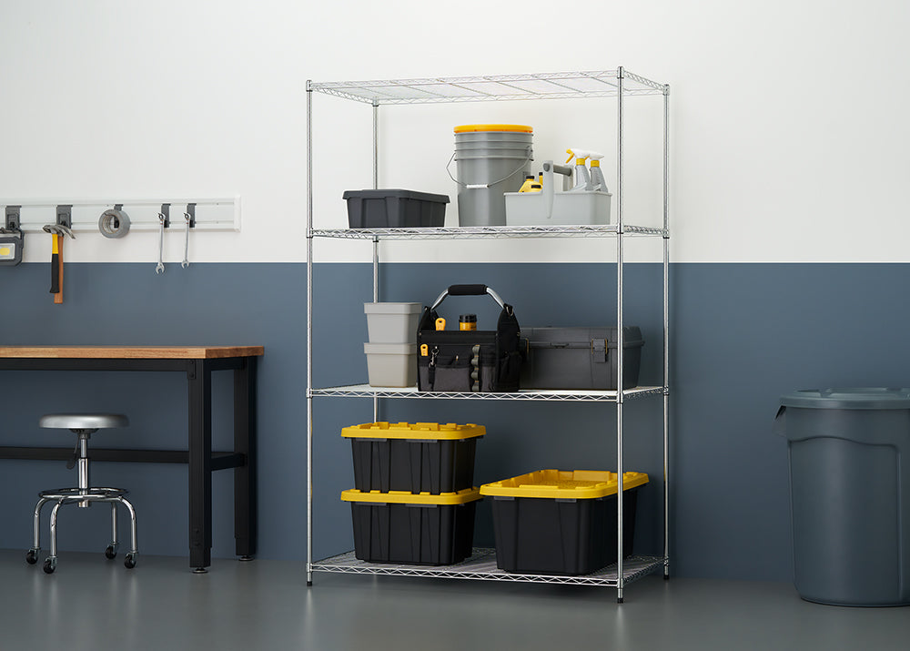 A well-organized garage or workshop space is shown, featuring a five-shelf chrome wire shelving unit stocked with various storage containers, a tool tote, and buckets. To the left is a wooden-top workbench with a metal frame, a rolling stool, a magnetic tool rail with hand tools, and a large trash can to the right, all set against a white and gray wall.