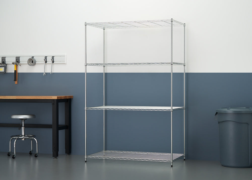 An empty five-tier chrome wire shelving unit stands against a two-tone white and blue wall in a garage-like setting. To the left is a wooden workbench with tools hanging on a rail above it, and to the right is a large grey plastic storage bin.