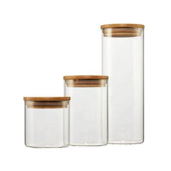 Three clear glass canisters of varying heights stand side-by-side, each sealed with a round, light brown bamboo lid. The canisters are empty and isolated against a plain white background.