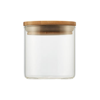 A clear, small cylindrical glass jar is shown with a round, light brown wooden lid resting on top. The minimalist design highlights the transparency of the glass and the natural texture of the bamboo lid.
