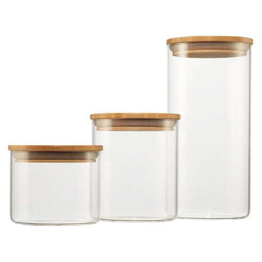 Three clear glass canisters of varying heights stand side-by-side, each sealed with a round, light brown bamboo lid. The canisters are empty and isolated against a plain white background.