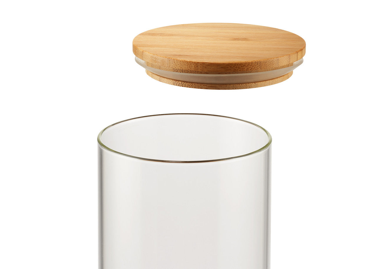 A clear, cylindrical glass container is shown with a round, light brown wooden lid hovering above it. The lid has a clear silicone or plastic ring around its edge where it would meet the glass.