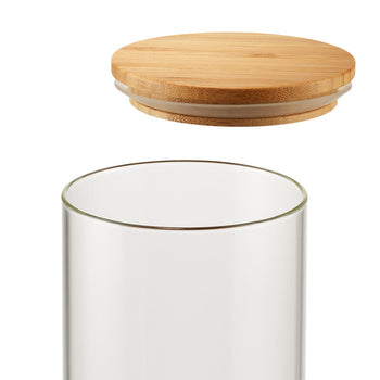 A clear, cylindrical glass container is shown with a round, light brown wooden lid hovering above it. The lid has a clear silicone or plastic ring around its edge where it would meet the glass.