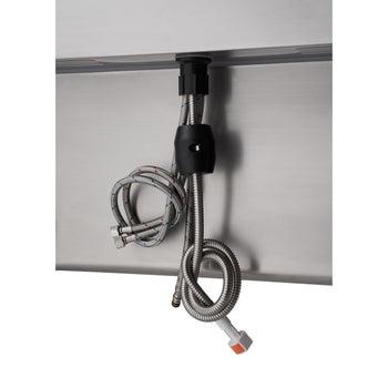 A close-up shows the underside of a stainless steel sink with a pull-out faucet mechanism. Two braided metal hoses hot and cold water line extend downwards, secured by black plastic clips to the bottom of the sink basin.