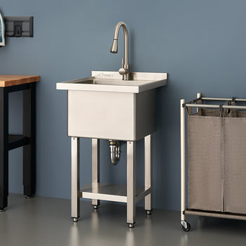 A stainless steel utility sink with a tall gooseneck faucet stands in a modern laundry room or workshop between a wooden workbench and a rolling laundry sorter. The scene is set against a dark blue wall and features clean, industrial-style organization.
