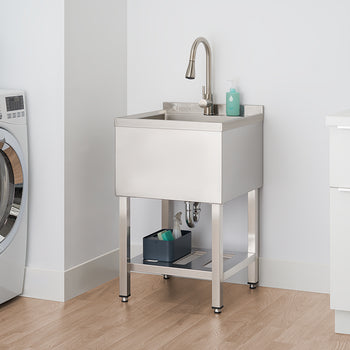 A polished stainless steel utility sink with a gooseneck faucet stands in a laundry room. Cleaning supplies are stored on a shelf beneath the sink, next to a white washing machine.
