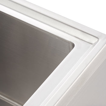 A close-up, high-angle shot shows the top right corner of a brushed stainless steel rectangular sink. The sink has crisp, clean lines and a subtle, polished sheen, suggesting a modern and functional design.