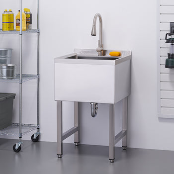A chrome utility sink with a faucet stands against a white wall in a well-organized garage or workspace. To the left, a metal shelving unit holds various items including buckets and storage bins, while tools and a yellow extension cord hang on a pegboard to the right.