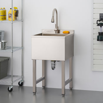 A freestanding stainless steel utility sink with a tall gooseneck faucet is centered against a white wall in a clean garage or workshop setting. The scene includes a wire shelving unit with storage bins to the left and a wall-mounted tool organizer with various hardware to the right.