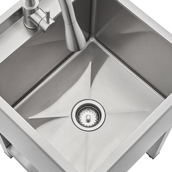 An overhead view of a square, brushed stainless steel utility sink basin featuring an X-shaped drainage groove leading to a center drain. The image shows the internal depth of the sink, the base of a single-handle faucet, and the Trinity Basics logo on the back ledge.