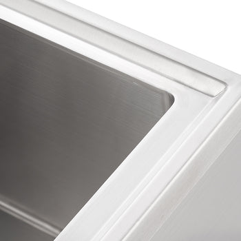 A close-up, high-angle shot shows the interior of a stainless steel sink, highlighting its brushed finish and clean lines. The top edge of the sink features a subtle, raised lip, and the inner corners are smoothly curved.