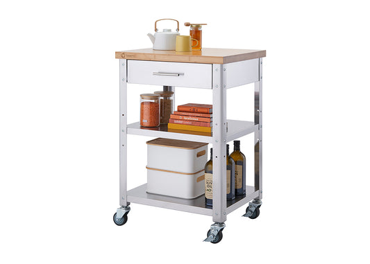 A modern kitchen cart with a stainless steel frame, a wooden top, and four caster wheels. The cart features a drawer, two shelves stocked with kitchen essentials such as jars of lentils, cookbooks, storage containers, and bottles of olive oil.