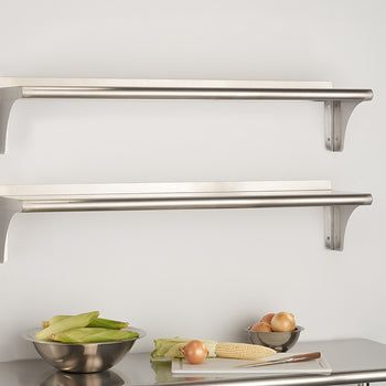 Two stainless steel rectangular bracket shelves are mounted on a white wall above a stainless steel countertop. Bowls of vegetables and a cutting board with an onion and corn are on the counter below.