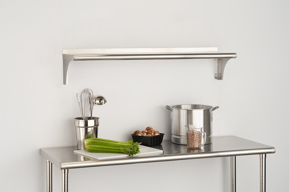 A stainless steel wall shelf is mounted above a stainless steel table, both holding various kitchen items. The shelf features a horizontal bar, and the table displays a cutting board with celery, a pot, and other cooking utensils.