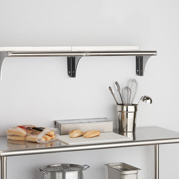 A stainless steel utility table with a lower shelf is shown in the foreground. A wall-mounted shelf with a backsplash is visible above, and various kitchen items are arranged on both surfaces.
