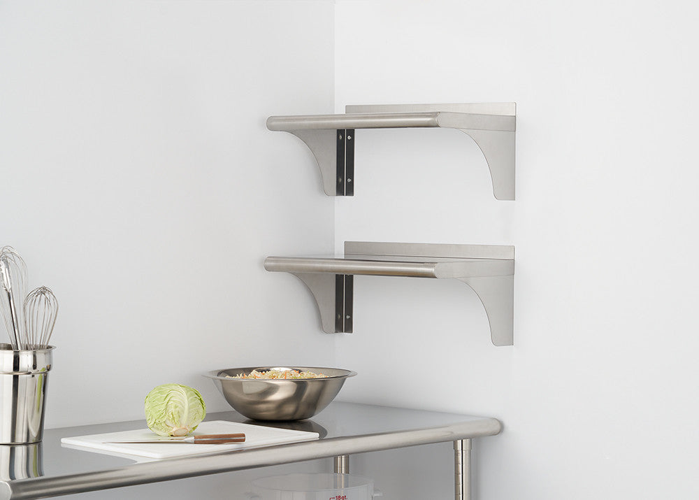 Two stainless steel shelves are mounted on a white wall in a corner. Below the shelves, a stainless steel prep table holds a cutting board with a knife and a halved head of cabbage, along with a stainless steel mixing bowl.