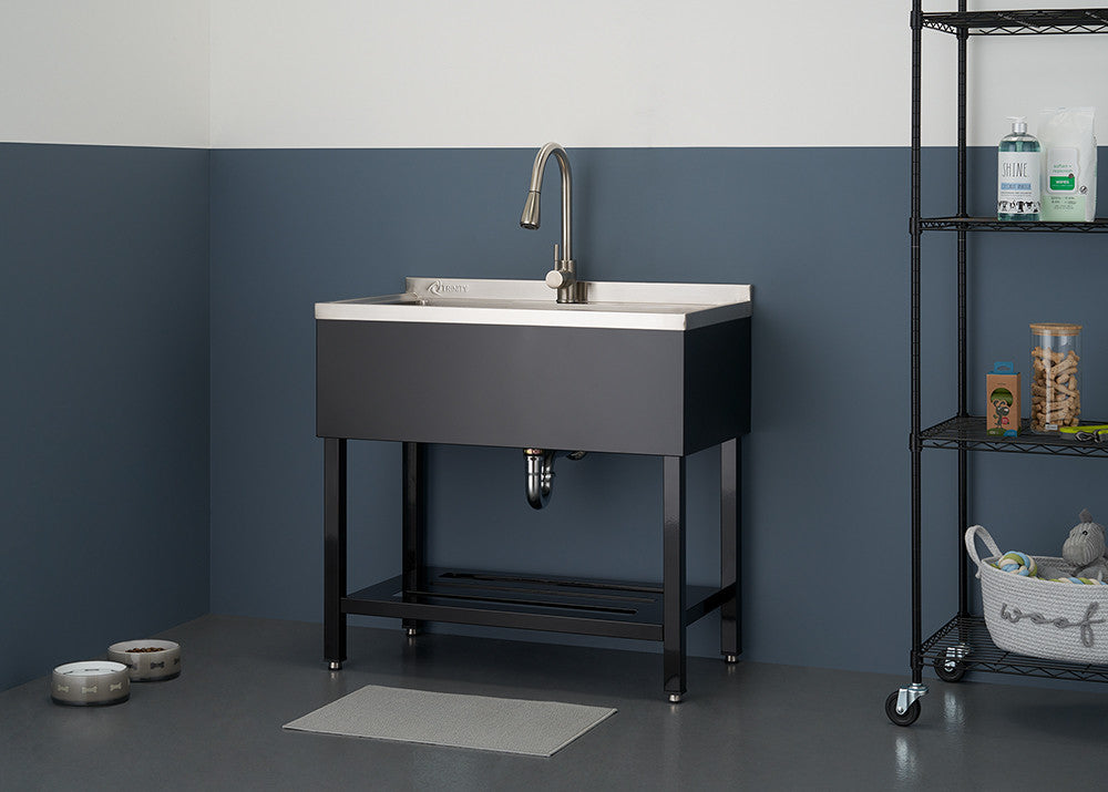 A stainless steel utility sink with a brushed metal faucet is centered in the frame, against a two-tone blue and white wall. To the right, a black wire shelving unit holds various cleaning supplies and a basket.
