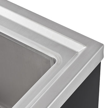A close-up shot shows the corner of a stainless steel utility sink, highlighting the smooth, reflective surface and the clean lines of its design. The sink appears to be mounted on a dark surface, possibly a countertop or cabinet, which provides a stark contrast to the metallic sheen.