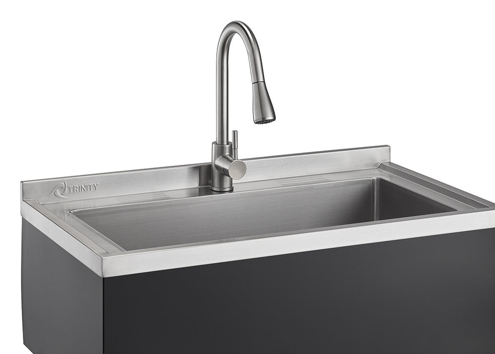 A close-up shot of a stainless steel utility sink with a pull-out faucet, featuring the "Trinity" brand logo on the backsplash. The sink is set in a dark-colored base, and the image highlights the clean lines and modern design of the fixture.