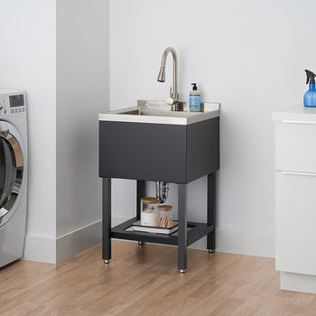 A modern laundry room features a black utility sink with a stainless steel faucet and basin, standing on sleek black legs. To the left is a white front-loading washing machine, and to the right, a white cabinet with an ironing board and spray bottle on top.