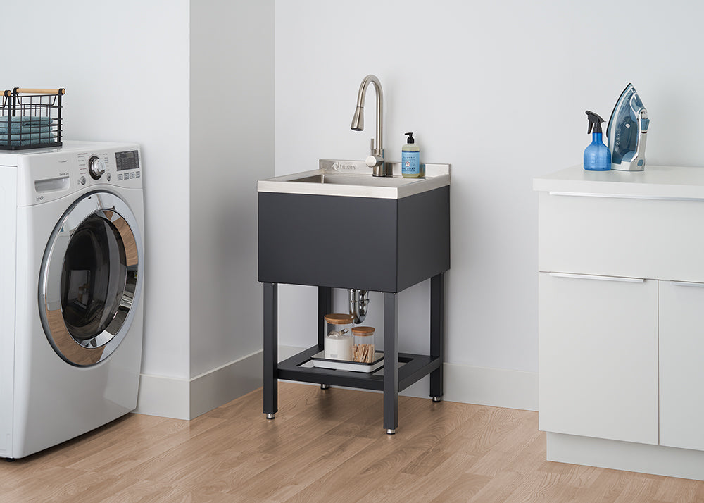 A modern laundry room features a black utility sink with a stainless steel faucet and basin, standing on sleek black legs. To the left is a white front-loading washing machine, and to the right, a white cabinet with an ironing board and spray bottle on top.