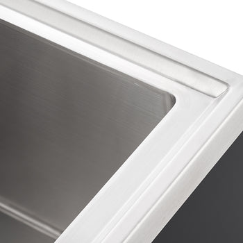 A close-up, high-angle shot shows the top right corner of a stainless steel kitchen sink. The sink has a brushed metal finish and a sleek, modern design.