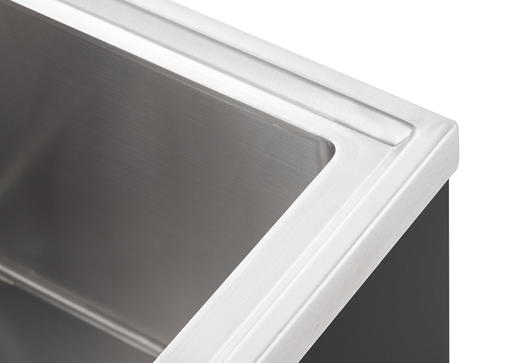 A close-up, high-angle shot shows the top right corner of a stainless steel kitchen sink. The sink has a brushed metal finish and a sleek, modern design.