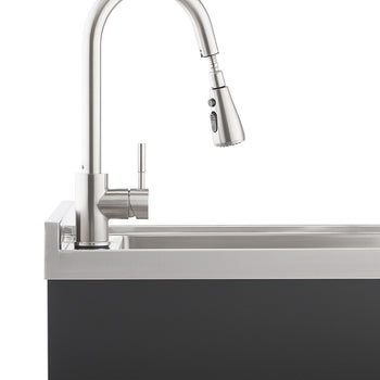 A modern brushed stainless steel gooseneck faucet with a pull-down spray head is mounted on a stainless steel sink, which is integrated into a dark gray or black cabinet base. The faucet is positioned prominently against a white background, highlighting its sleek design.