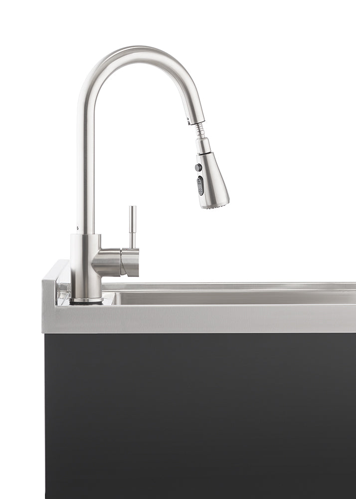 A modern brushed stainless steel gooseneck faucet with a pull-down spray head is mounted on a stainless steel sink, which is integrated into a dark gray or black cabinet base. The faucet is positioned prominently against a white background, highlighting its sleek design.
