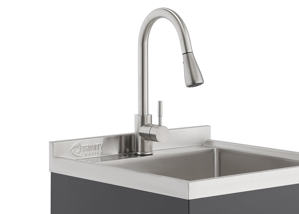 A close-up shot shows a stainless steel Trinity Basics sink with a modern, brushed nickel gooseneck faucet. The faucet features a pull-down sprayer head and a single handle control.